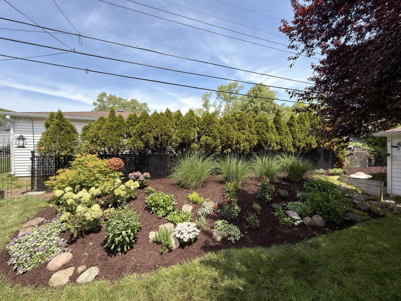 Layered planting bed with flowering shrubs and stone edging along a front walkway