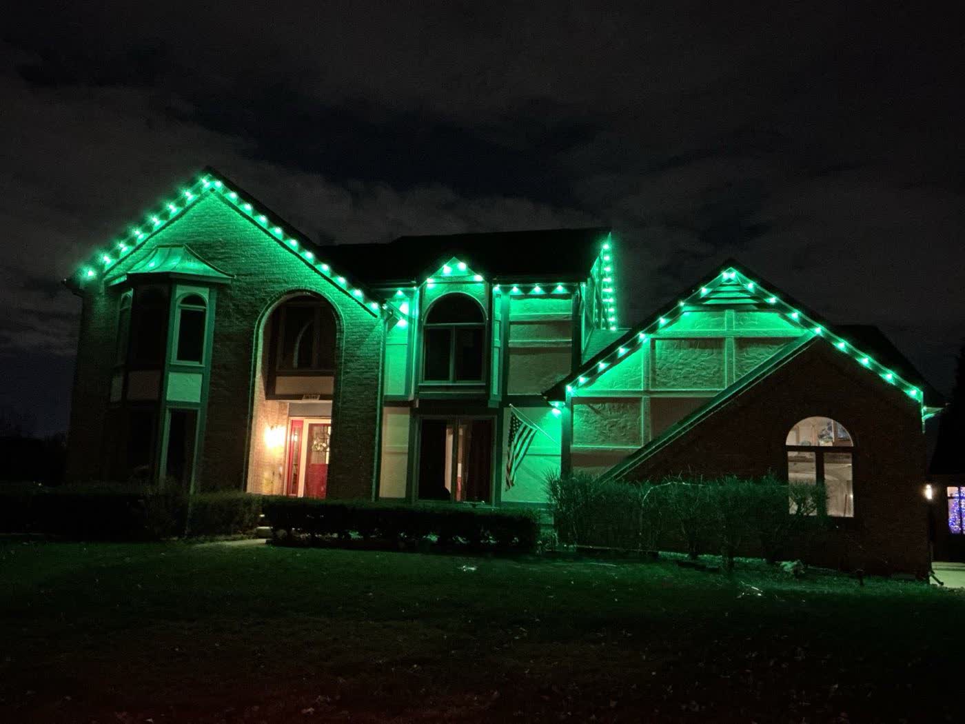 Green holiday roofline lighting installation on a home at night