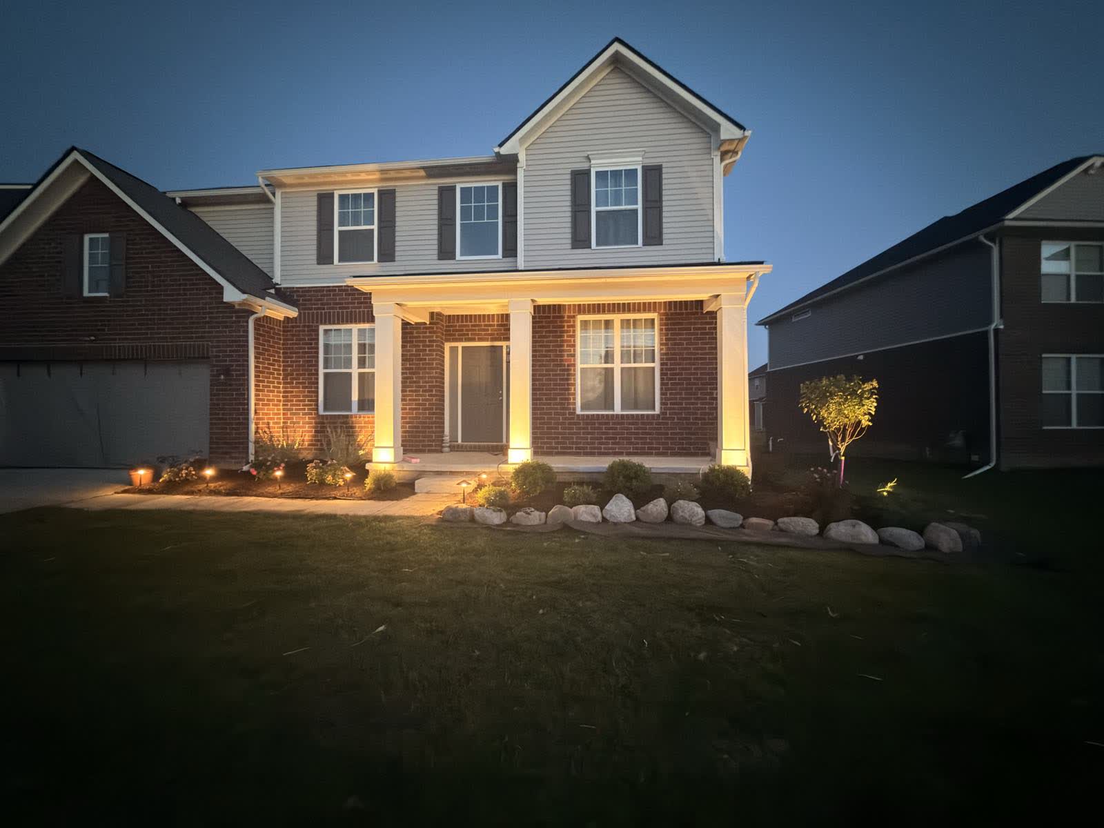 Full dark: porch columns washed with warm light and path lights running through the planting bed
